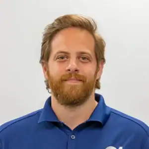 Flexible business professional with a friendly demeanor, wearing a blue polo shirt, standing against.