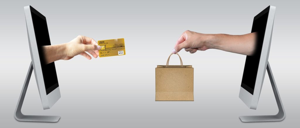 Two computer screens with hands coming out of them making an ecommerce store purchase