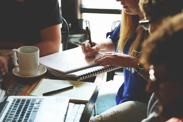 Team at a cafe table with laptops, coffee and notebooks, one person writing notes on the employee retention credit
