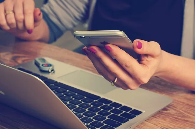 Woman holding a smartphone over an open laptop at a desk, considering who qualifies for ERC refunds