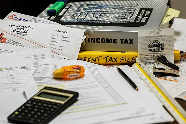Cluttered desk of tax invoices, an income tax binder, calculator and pens, explaining the Employee Retention Credit
